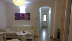 A modern living room with a white sofa, a dining table, and a painting of a rose. - BB Il Quadrifoglio (San Vito dei Normanni)