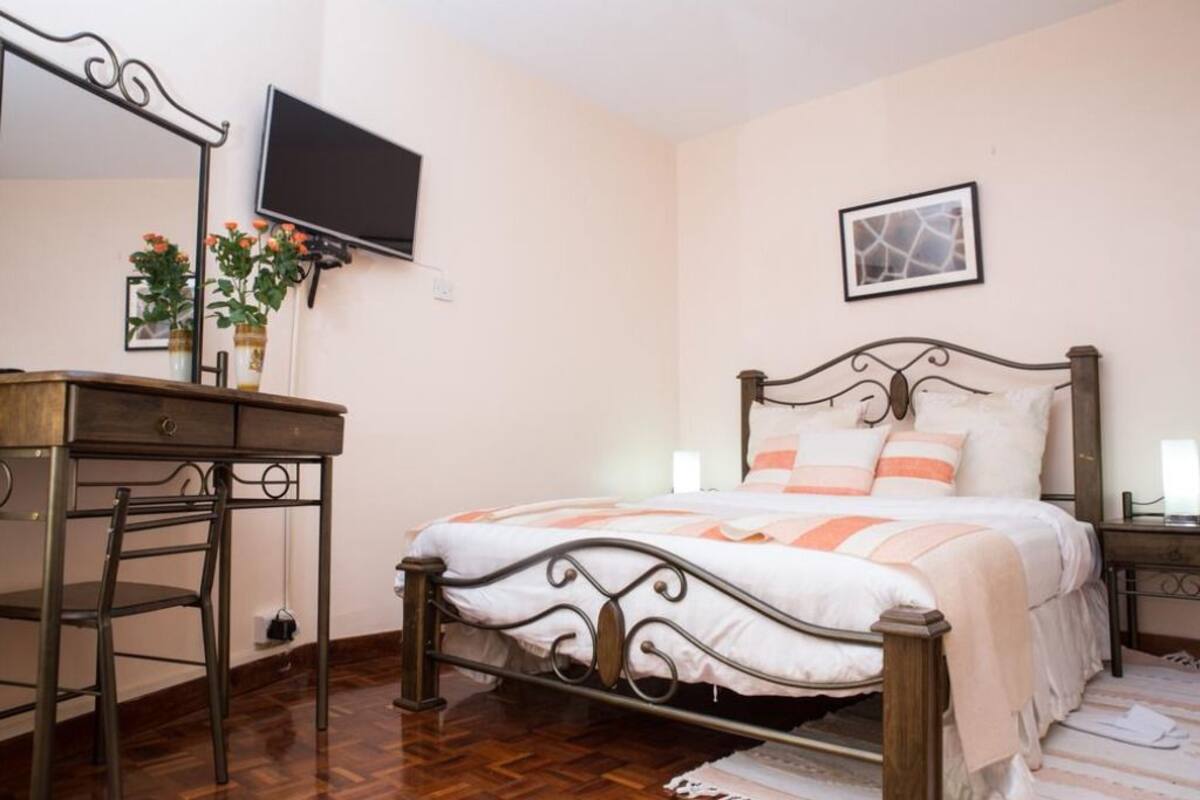 A bedroom with a bed, a desk, a chair, a television, and a framed picture on the wall.