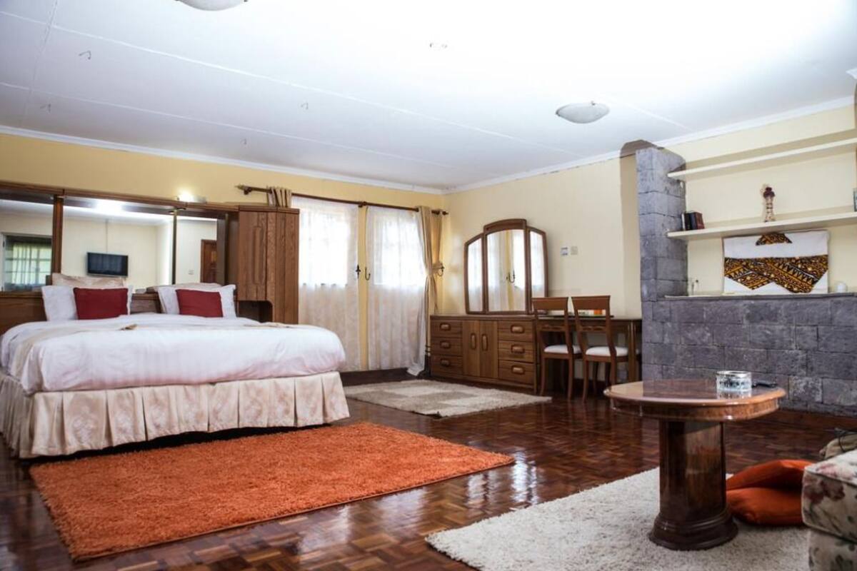 A bedroom with a large bed, a dresser, a mirror, a round table, and a fireplace.