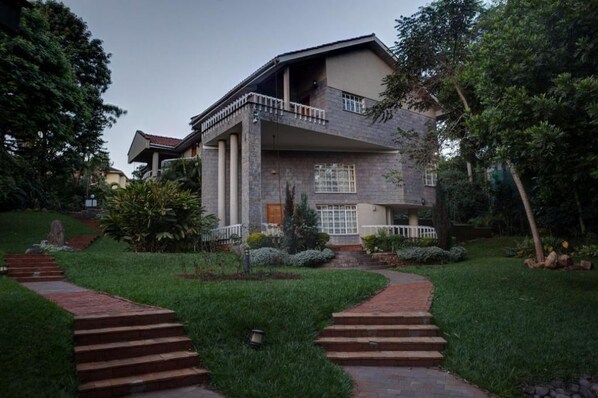A two-story house with a balcony, surrounded by a well-maintained garden and a stone pathway leading to the entrance.
