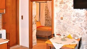 Une pièce chaleureuse avec un mur en pierre, un plafond en bois, un lit à baldaquin, un téléviseur fixé au mur et une table à manger avec des chaises.