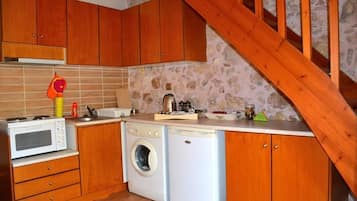 Een kleine keuken met houten kastjes, een magnetron, een wasmachine en een houten trap.