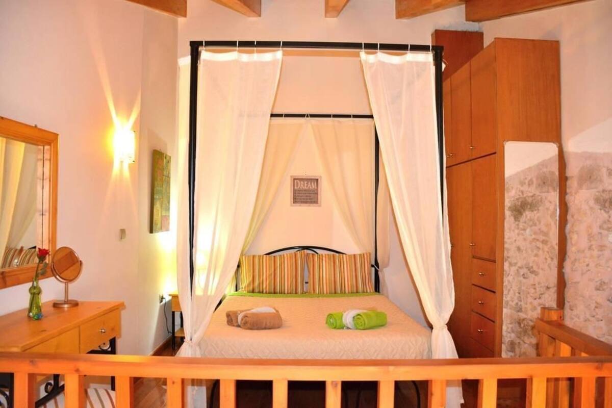 A bedroom with a canopy bed, wooden furniture, a mirror, and a wall-mounted light.