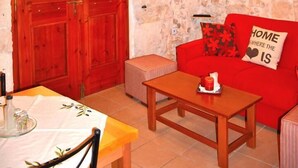 Une pièce chaleureuse avec un mur en pierre, une porte en bois et un canapé rouge agrémenté d’un coussin sur lequel est brodé le mot « FOYER ».