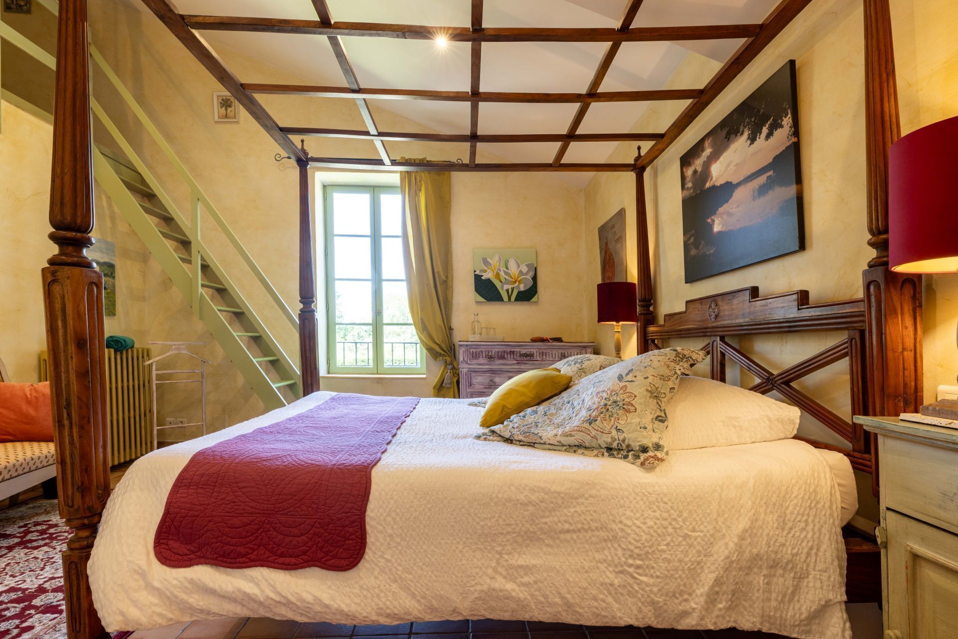 Une chambre à coucher avec un lit à baldaquin, un escalier en bois, une fenêtre avec des rideaux et un tableau accroché au mur.