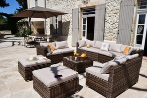 Relax in the outdoor seating area with wicker sofas and ottomans, a table, and chairs under a shaded umbrella.