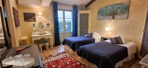 Two single beds with dark blue bedding, a desk with a chair, and a large window with blue curtains.