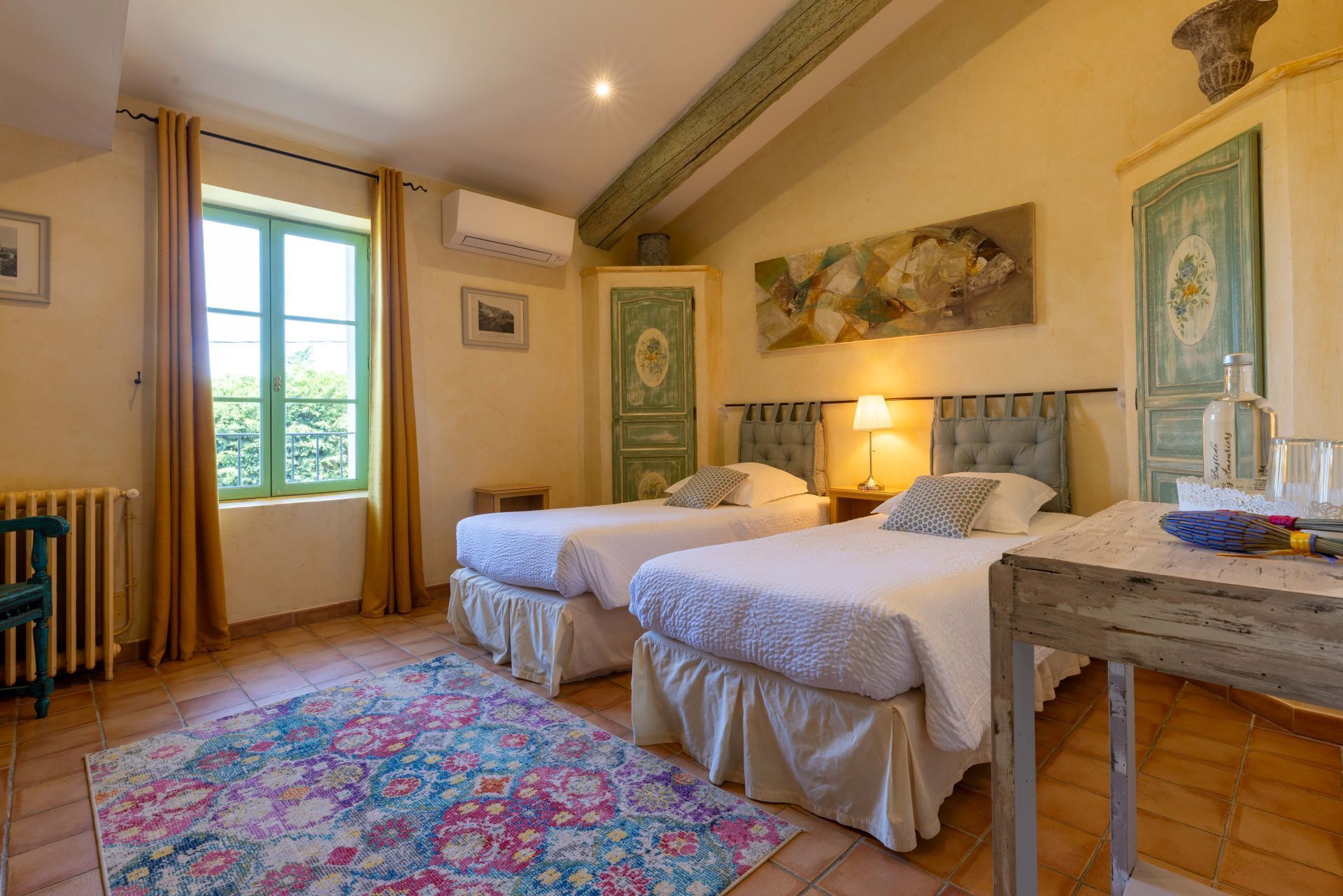 Une chambre avec deux lits, un radiateur, une fenêtre avec des rideaux, un appareil de climatisation et un tableau au mur.