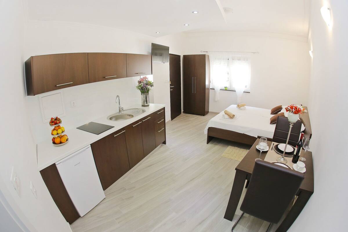 A compact hotel room with a kitchenette, a bed, a dining area, and a bathroom.