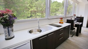 A modern kitchen with a large window, a sink, and a dining area with a table and chairs. - Deluxe Mkc Apartments (Zadar)