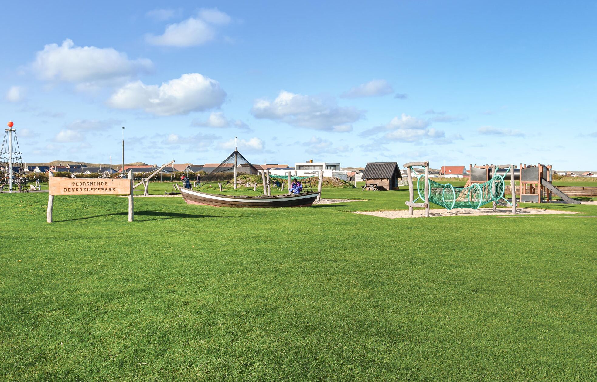 A grassy area with a boat, swings, and a sign that reads "Thorsminde Bevgelsespark".