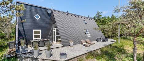 Ein modernes Haus mit Satteldach, einer Terrasse und Gartenmöbeln sowie einer Satellitenschüssel.