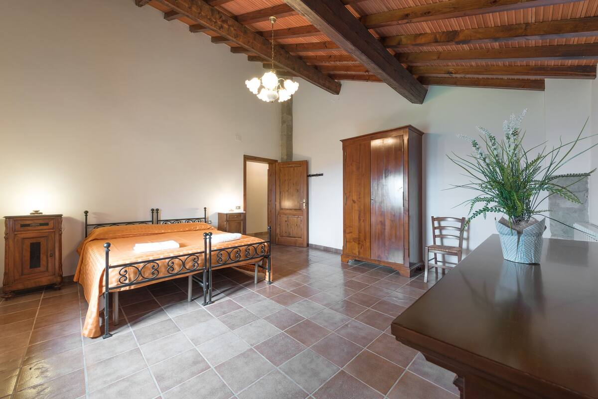 Un dormitorio con cama, armario de madera, mesita de noche y una planta en maceta.