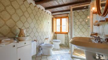 Une salle de bain avec un mur orné d’un motif hexagonal, un plafond en bois, une fenêtre, un lavabo, un bidet et des toilettes.