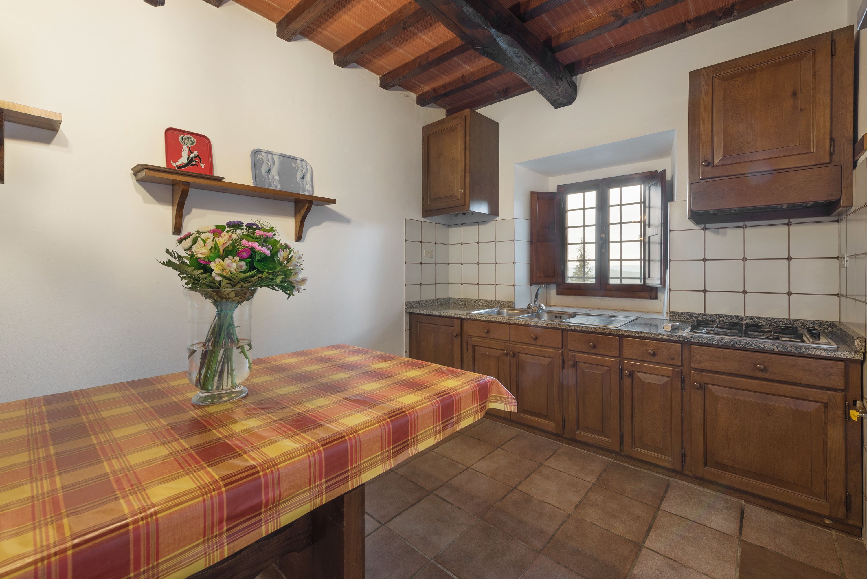 A kitchen with wooden cabinets, a tiled backsplash, a window, and a table with a plaid tablecloth.
