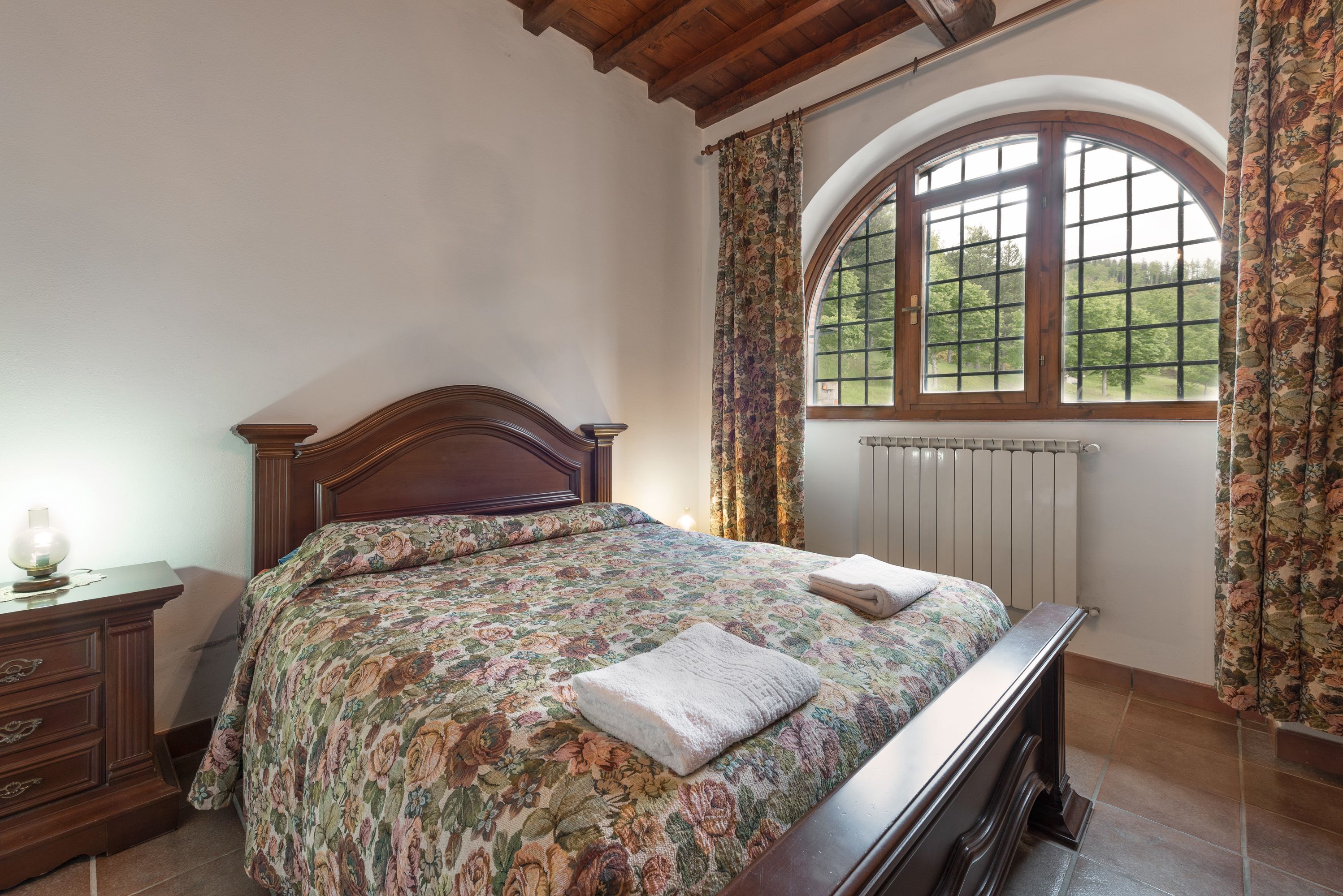 Una camera da letto con un letto di legno, copriletto floreale, un comodino e una finestra con tende.