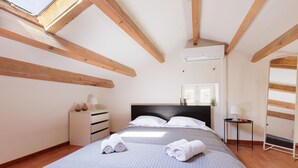Ein Schlafzimmer mit einem Bett, Holzbalken, einer Kommode, einem Nachttisch und einem Fenster.
