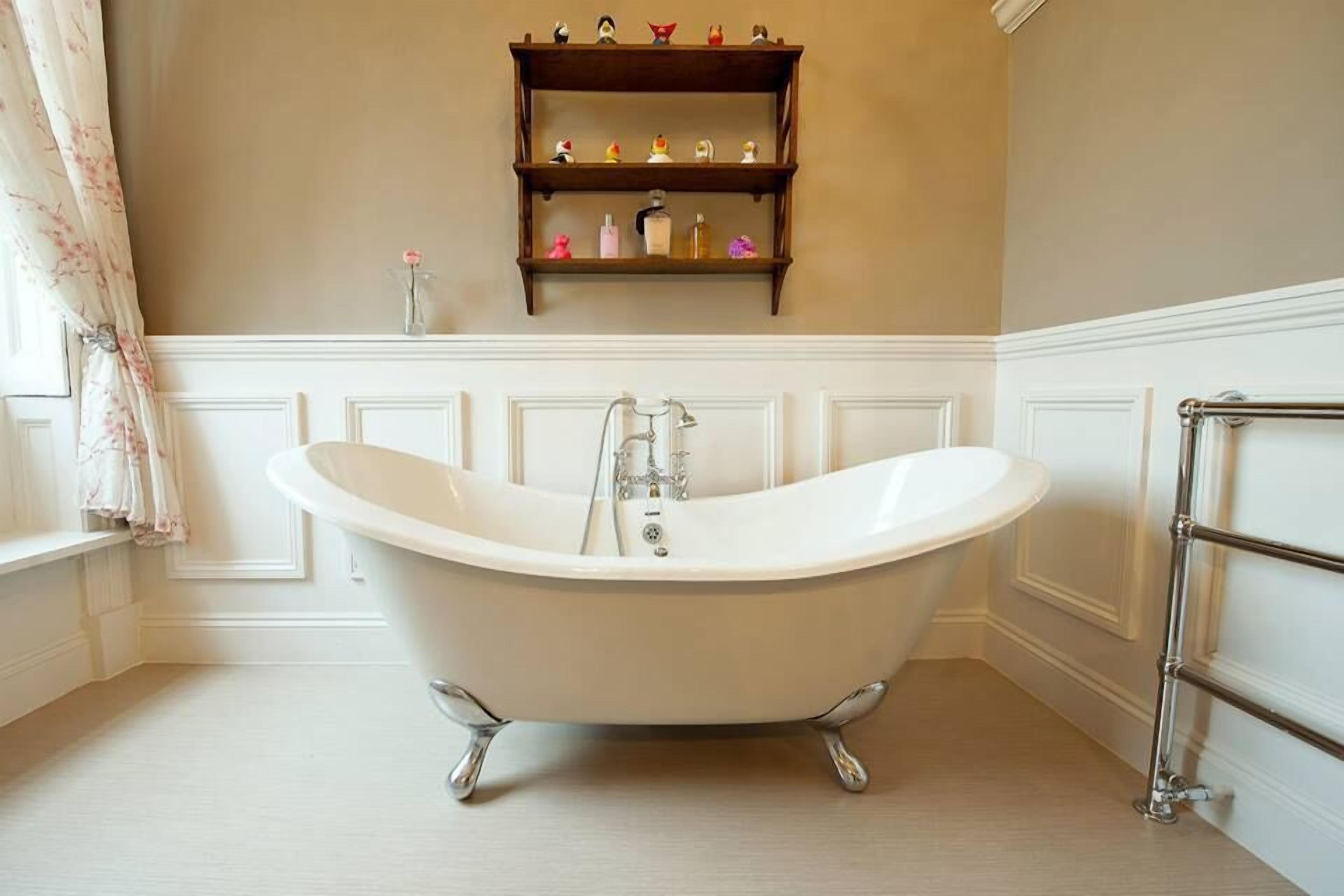 Ein Badezimmer mit einer freistehenden Badewanne, einem Holzregal mit Pflegeprodukten und einem Fenster mit Vorhängen.