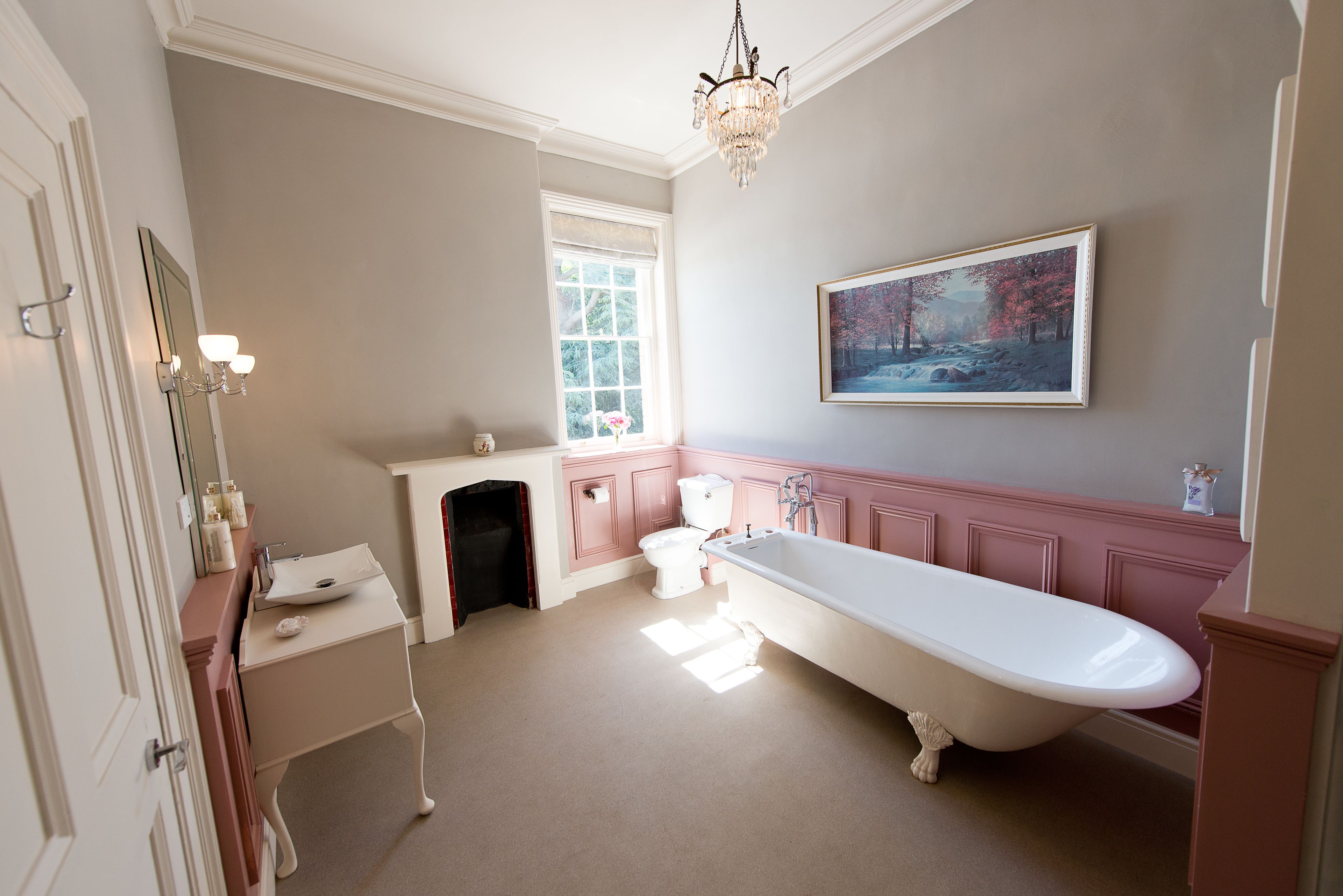 A bathroom with a clawfoot bathtub, a large mirror, and a painting on the wall.