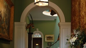 A grand hallway with a red carpet, a wooden staircase, and a large painting on the left. - Burton Court (Leominster)
