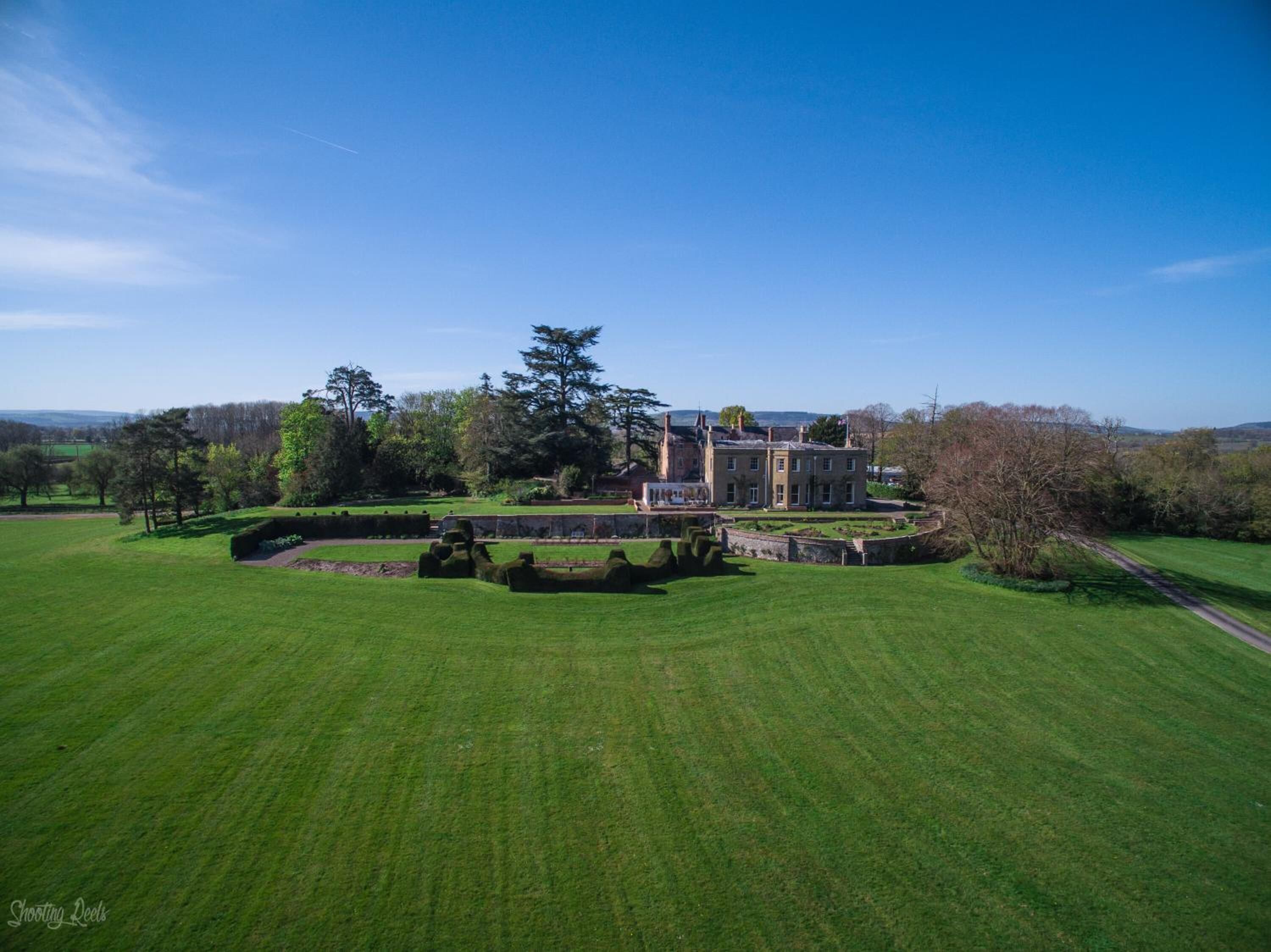 A large, historic building with a formal garden and a well-maintained lawn.