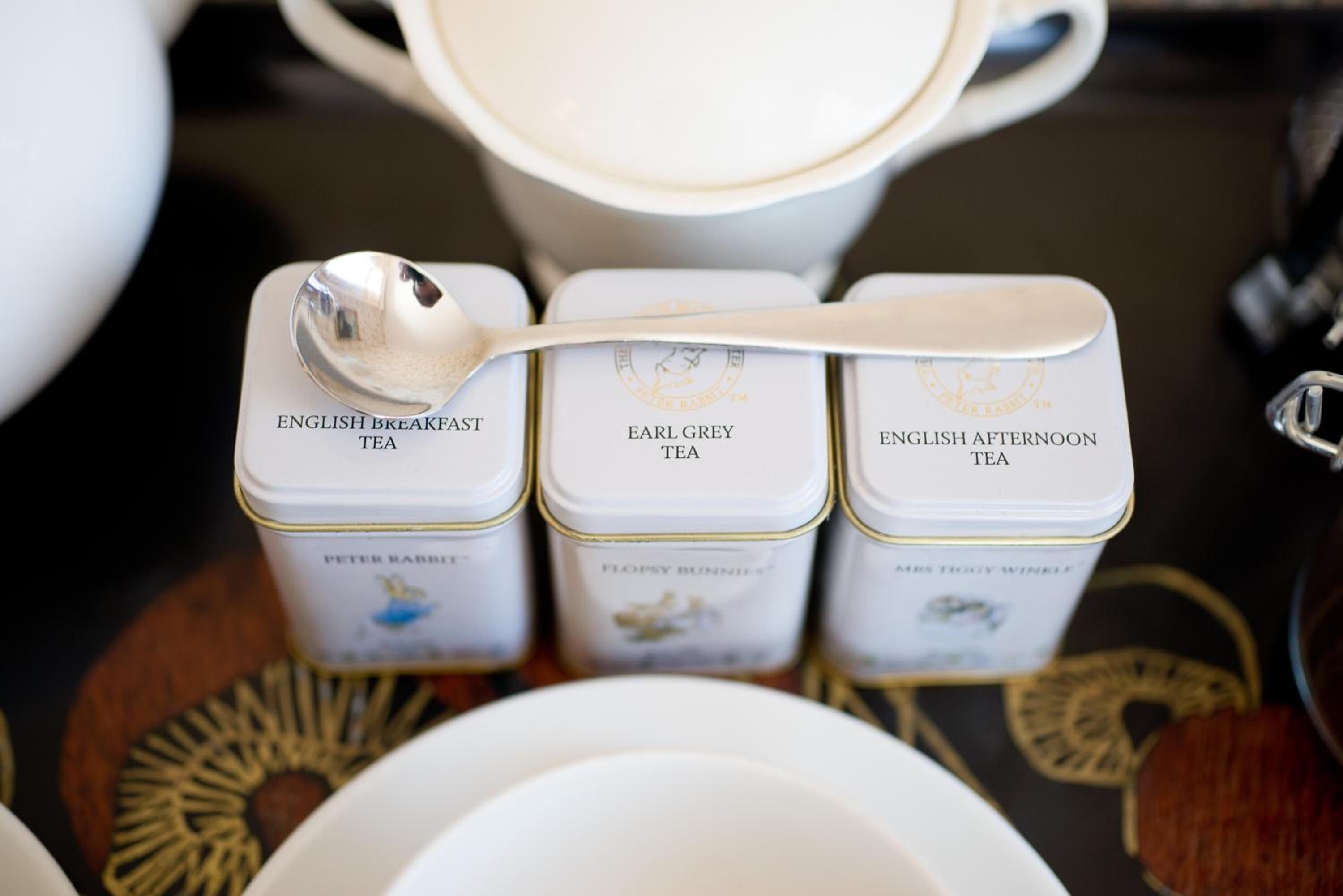 Tres latas de té con las etiquetas 'English Breakfast Tea', 'Earl Grey Tea' y 'English Afternoon Tea' sobre una mesa con una cuchara.