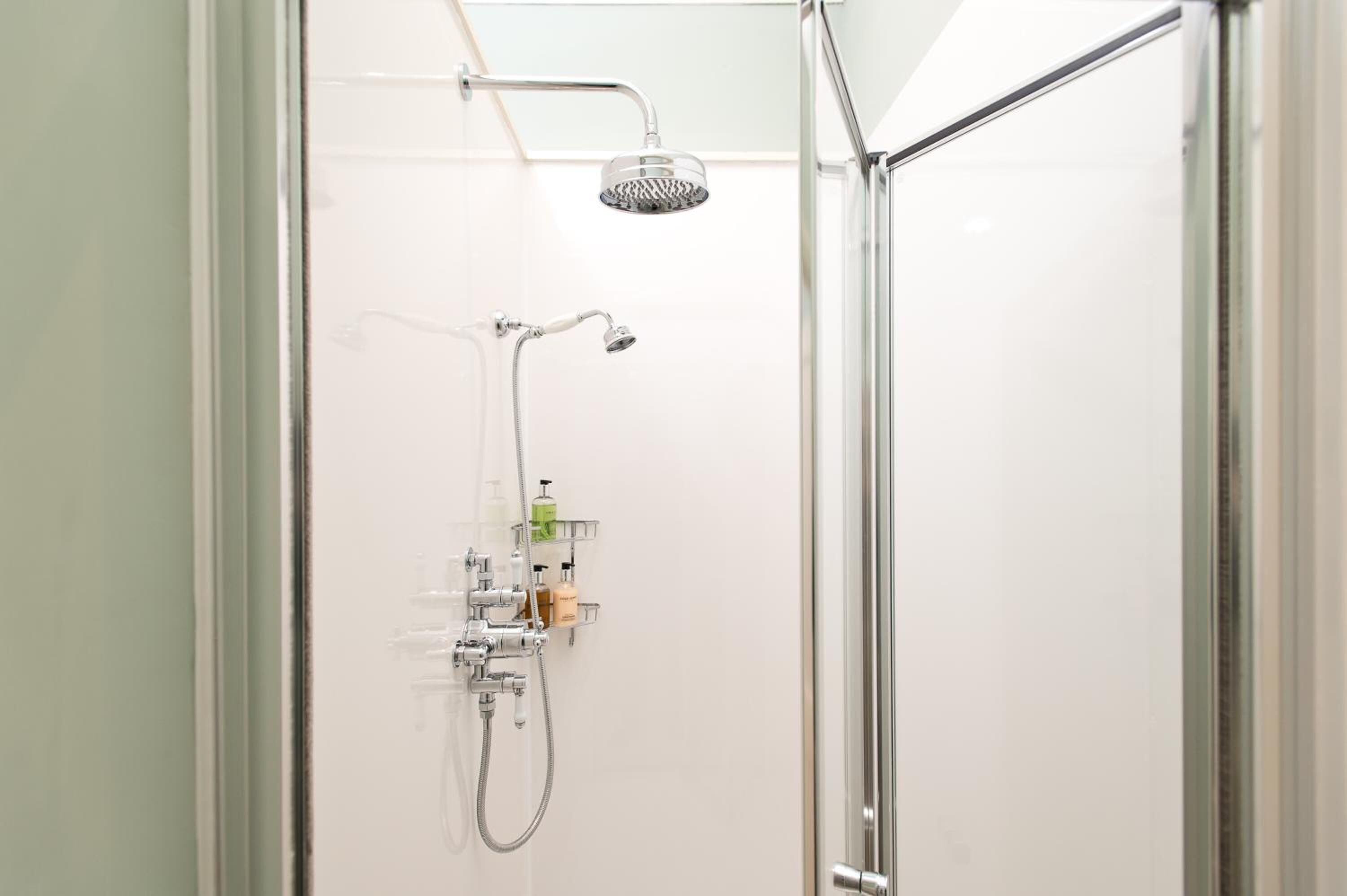 A modern shower with a handheld showerhead and a wall-mounted faucet, with toiletries on a shelf.