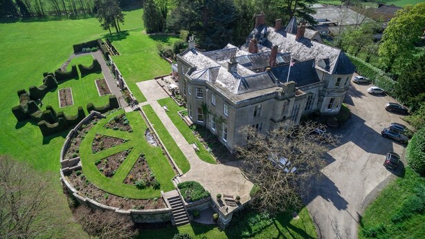 An aerial view of a large, historic building with a formal garden, a driveway, and parked cars. - Burton Court (Leominster)