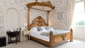A classic four-poster bed with a wooden frame and canopy, a bedside table with a lamp, and a nightstand with a lamp. - Burton Court (Leominster)