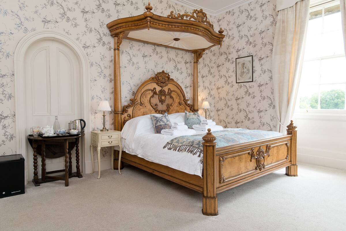 A classic four-poster bed with a wooden frame and canopy, a bedside table with a lamp, and a nightstand with a lamp.