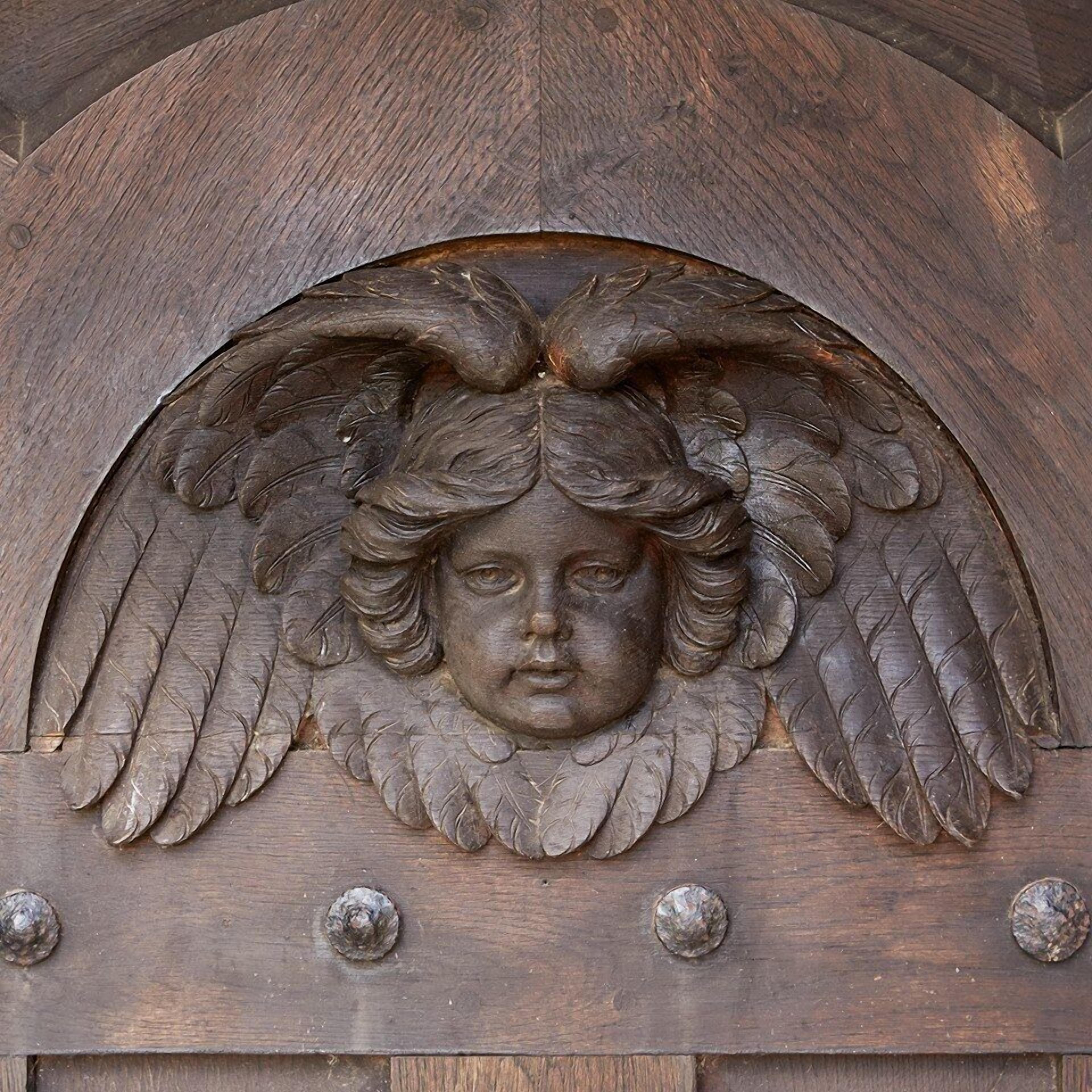 A wooden door with a carved angel head and wings.