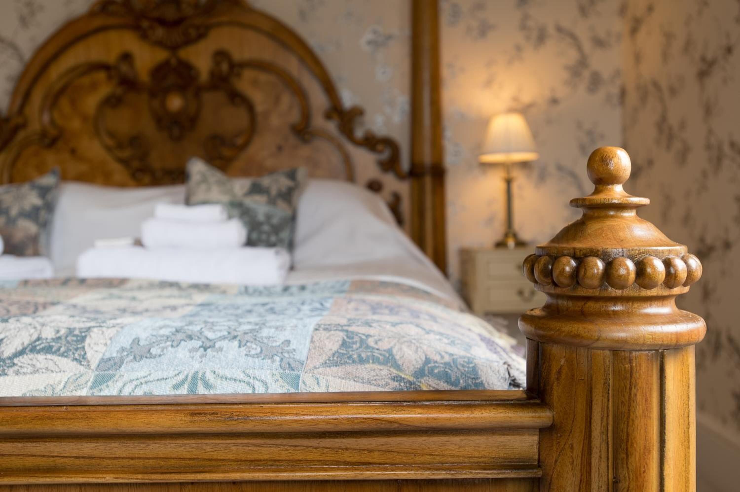 Un lit bien fait, avec une couvre-lit à motifs, une tête de lit en bois et une table de chevet surmontée d’une lampe.