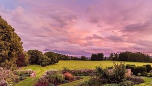 A landscaped garden with a variety of trees and shrubs, a well-maintained lawn, and a brick pathway. - Burton Court (Leominster)