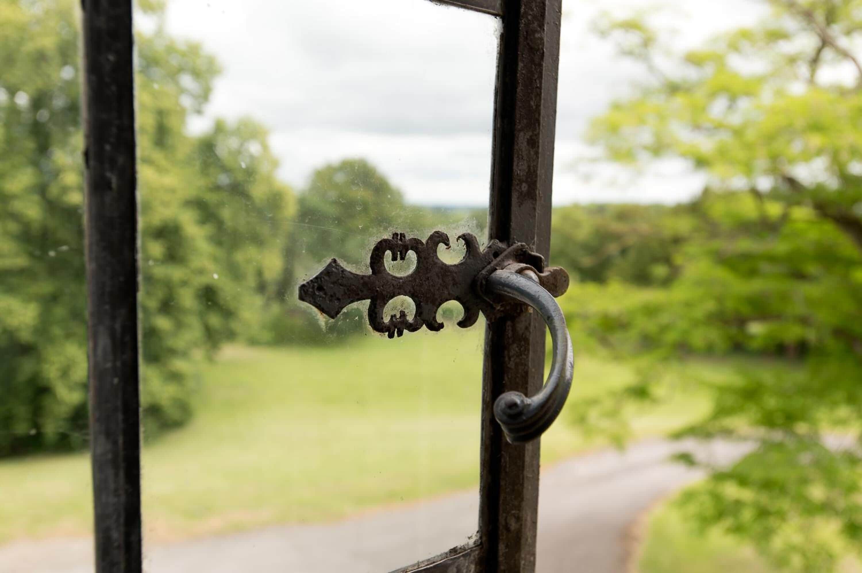 Een metalen deurklink met ingewikkelde decoraties, voor een onscherpe achtergrond van een groen landschap en een weg.