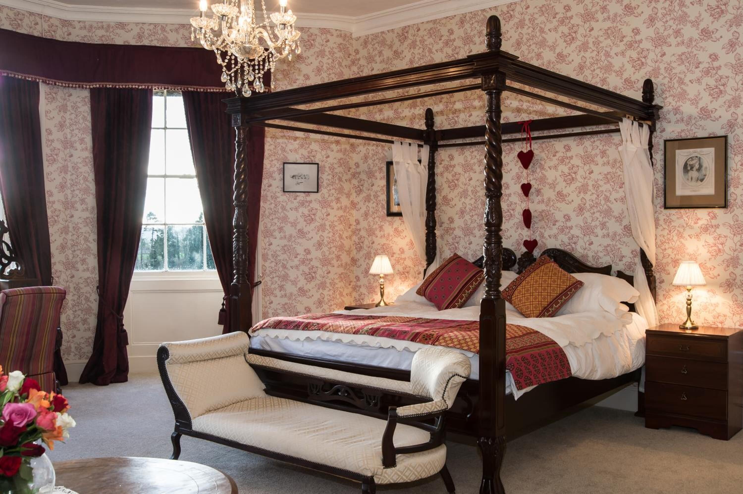 Ein Himmelsbett mit Baldachin, eine Liege, ein Nachttisch mit Lampe und ein gerahmtes Bild an der Wand.