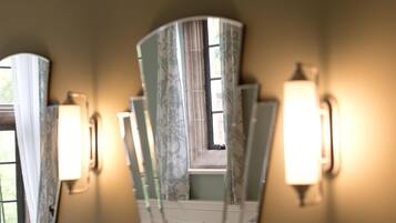 Una habitación con ventana, una lámpara en la pared y un espejo que refleja parte del espacio.