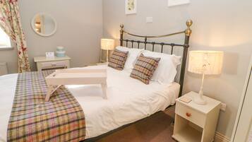 A neatly made bed with a plaid bedspread, two bedside lamps, and a nightstand with a lamp.