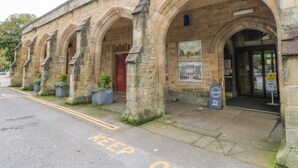 A stone building with arched doorways and a red door, featuring a 'KEEP CLEAR' sign on the pavement. - The Stable, Sedbury Park Farm (Richmond)