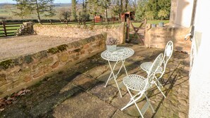 A patio with stone walls, a metal table and chairs, and a view of a rural landscape with trees and a fence. - The Stable, Sedbury Park Farm (Richmond)