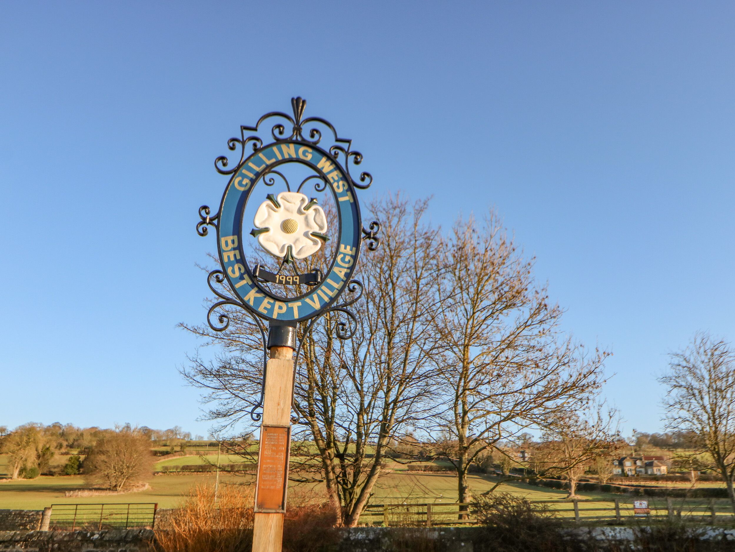 En skilteplade for en landsby med et blomsteremblem og teksten "BESTKEPT VILLAGE 1999".