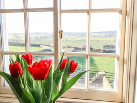 Una ventana con vistas a un paisaje verde y un arreglo de tulipanes rojos.