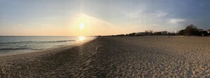 Una playa con cielo despejado y el sol poniéndose en el horizonte.