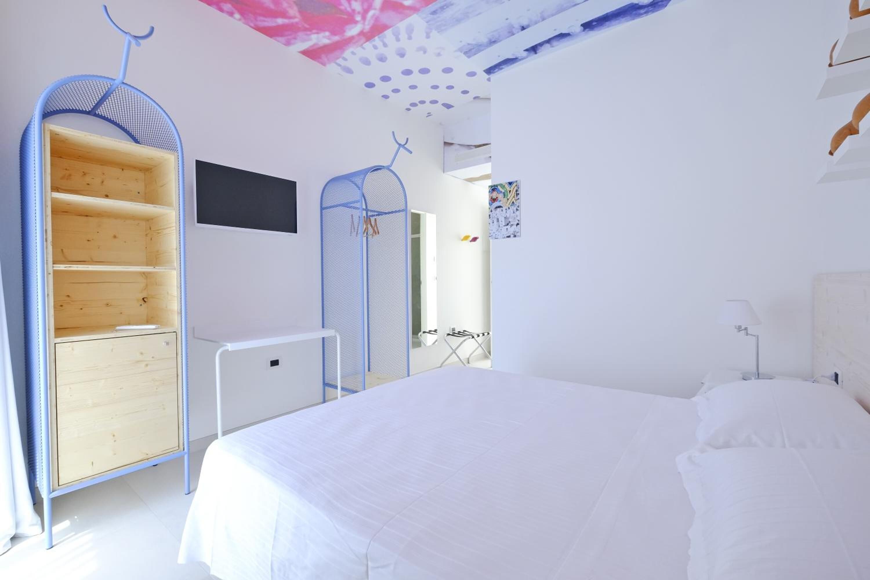 A bedroom with a large bed, a wardrobe with shelves, a desk, and a chair.
