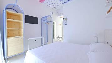 A bedroom with a large bed, a wardrobe with shelves, a desk, and a chair.