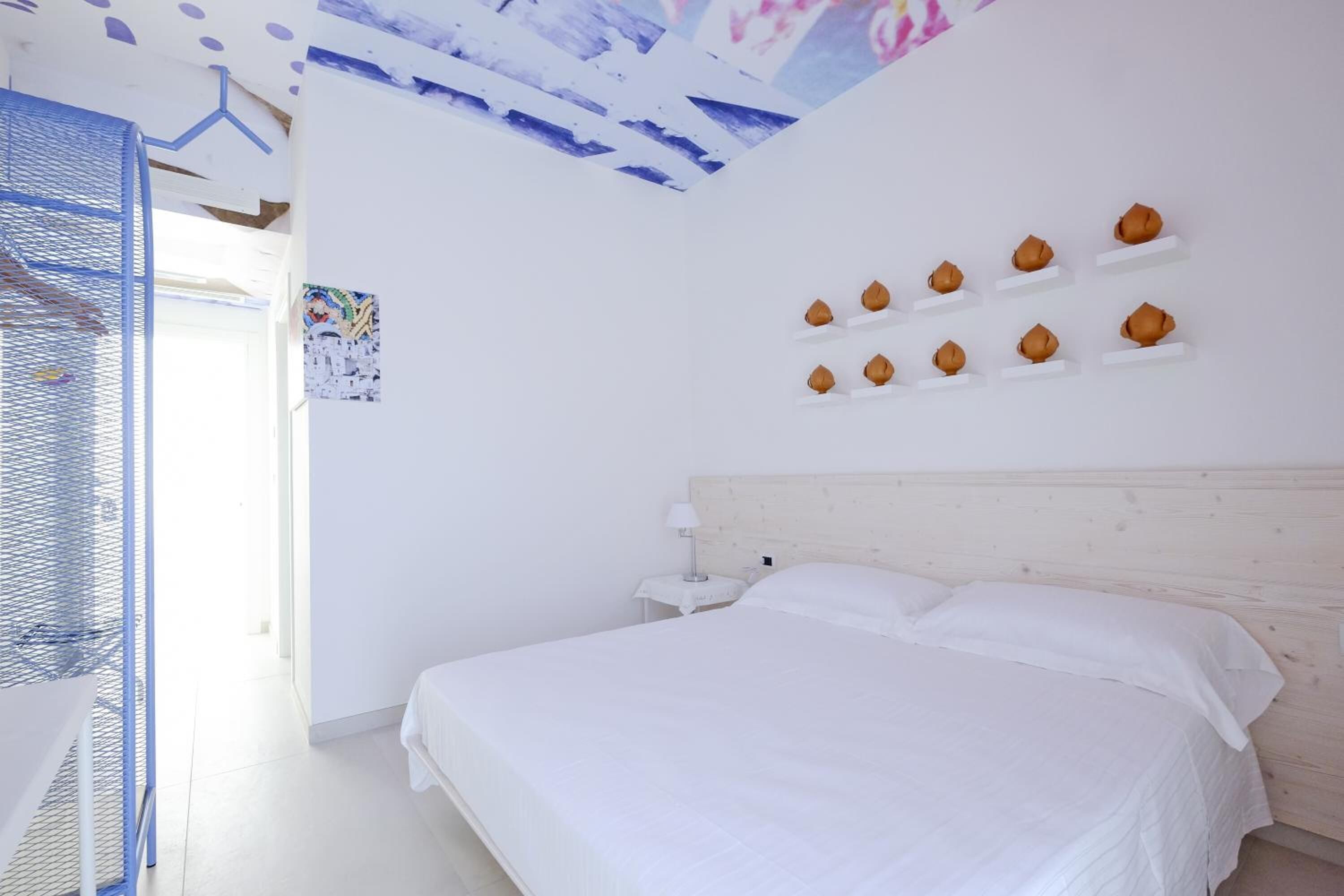 A bedroom with a large bed, a nightstand, and a wall-mounted shelf with decorative items.