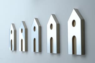 Cinco objetos con forma de casa, metálicos, alineados sobre una pared lisa.