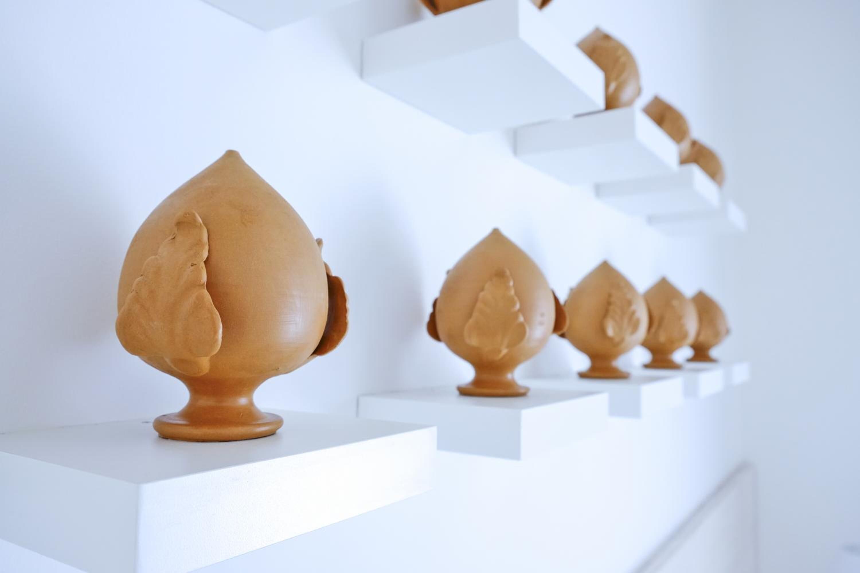 A series of ceramic objects on white shelves against a white background.