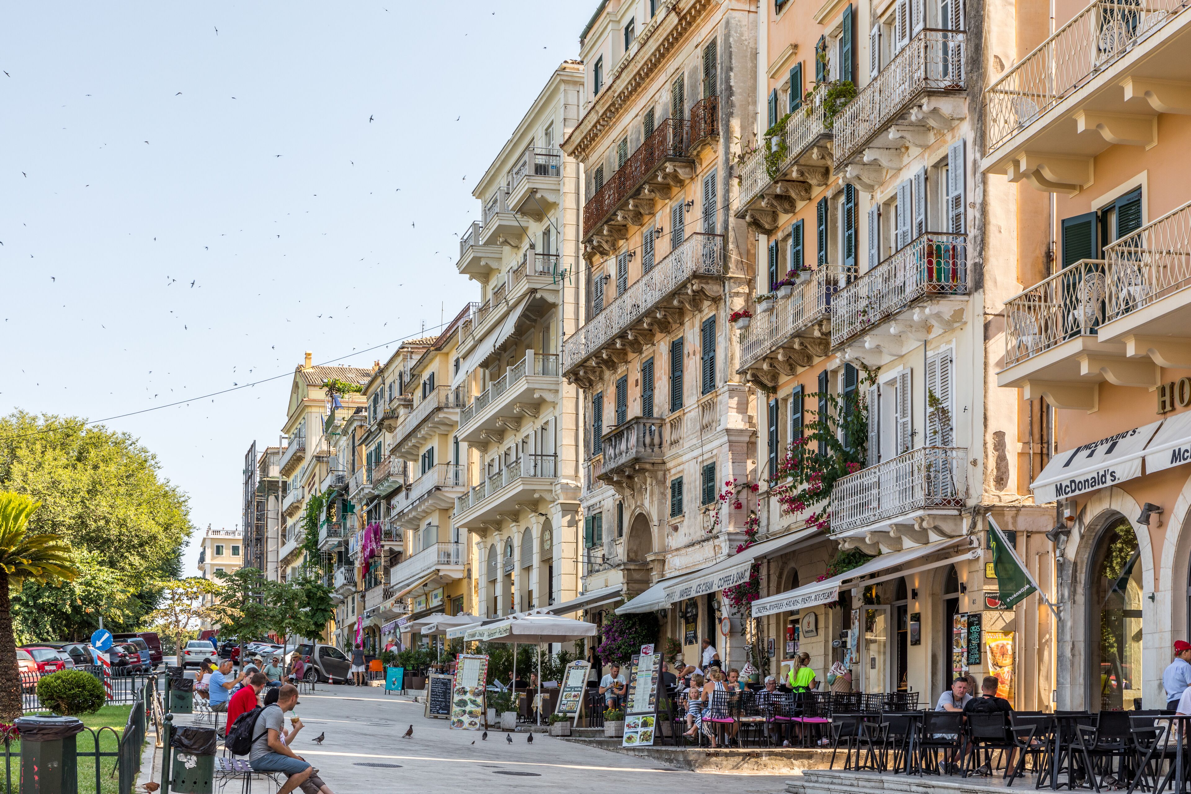 A street with outdoor seating at cafes, a McDonald's restaurant, and a variety of buildings with balconies and shops.