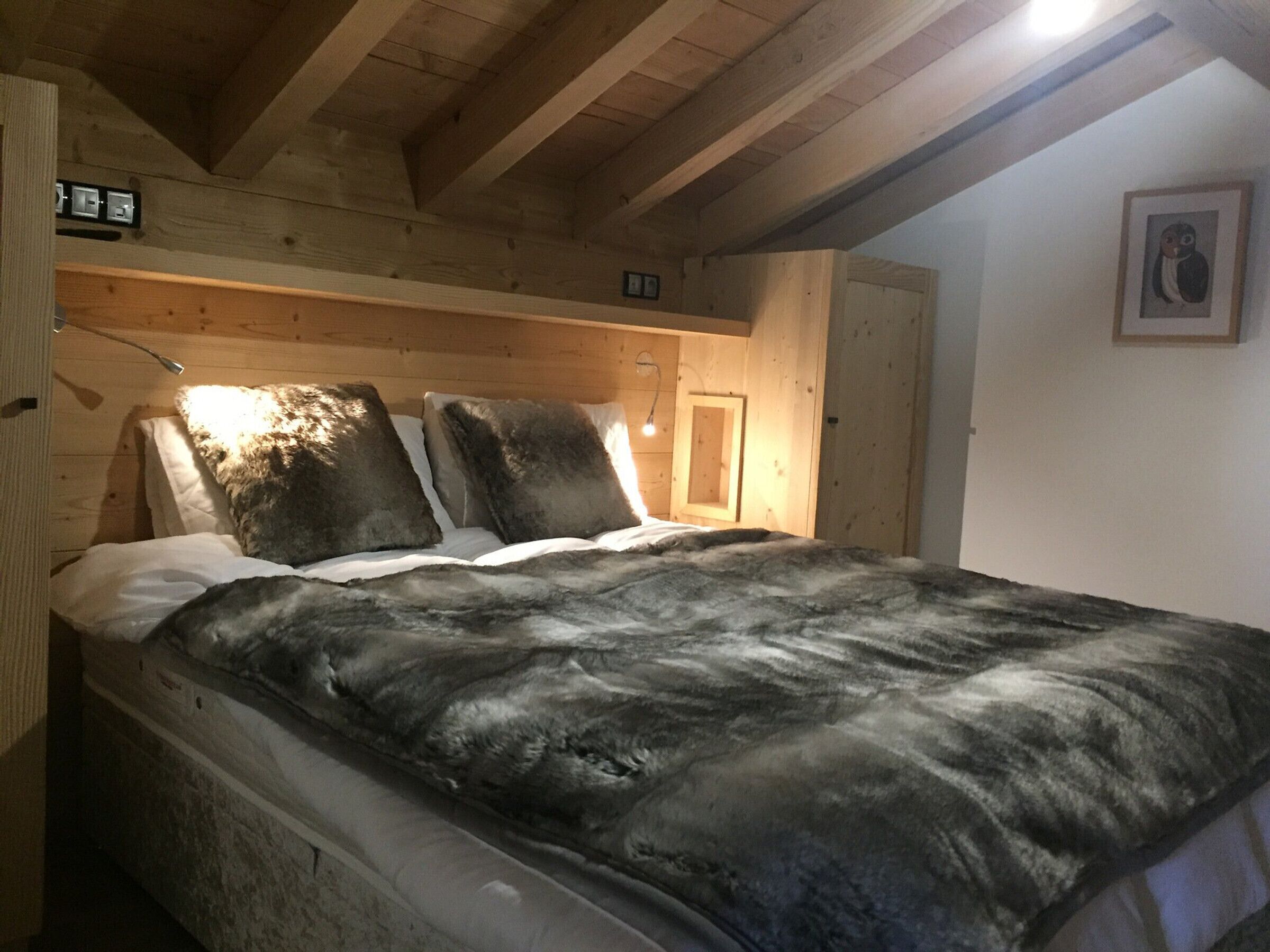 Un dormitorio de cabaña de madera con cama, almohadas y un cuadro en la pared.