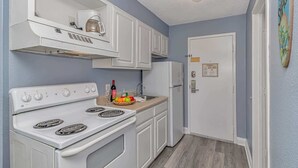 A compact kitchen with white appliances, a sink, and a door with a sign. - Sea Mist 51408 (Myrtle Beach)